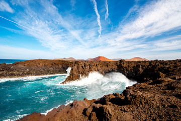 Los Hervideros rocky coast with wavy ocean and volcanos on the background on Lanzarote island in Spain