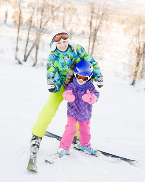 Mom and daughter while snow skiing showing thumbs up