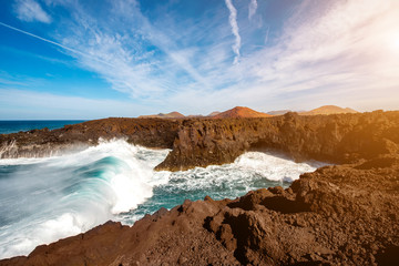Los Hervideros rocky coast with wavy ocean and volcanos on the background on Lanzarote island in Spain