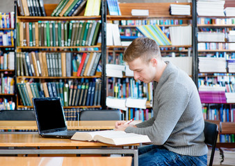 Male student with laptop studying in the university library