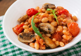 Stewed white beans with mushrooms and tomatoes with spicy sauce in a white bowl