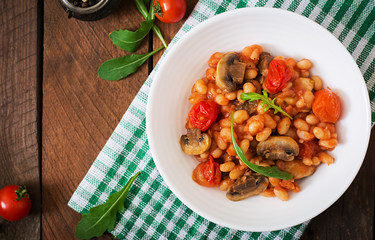 Stewed white beans with mushrooms and tomatoes with spicy sauce in a white bowl. Top view