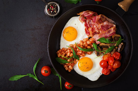 English breakfast - fried egg, beans, tomatoes, mushrooms, bacon and toast. Top view