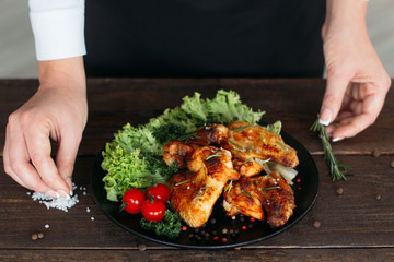 Top view of food decoration on wooden table. Chief presents grilled spicy chicken. Decorating chicken wings with lettuce and tomatoes cherry. 