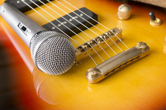 Electric guitar and microphone. Detail, focus on microphone and strings.