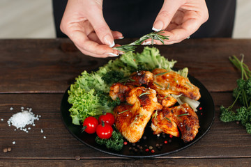 Food decoration on wooden table. Chief presents grilled spicy chicken. Decorating chicken wings with lettuce and tomatoes cherry. 