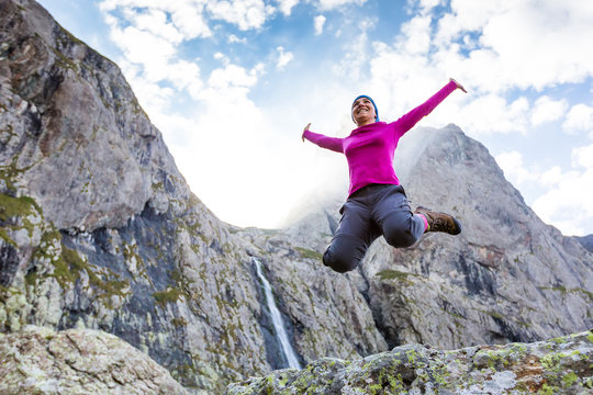 Woman trekker is standing against high mountains waterfall in Ca