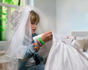 Teen girl trying on wedding dress and veil. The concept of early marriage, dreams of a wedding. 