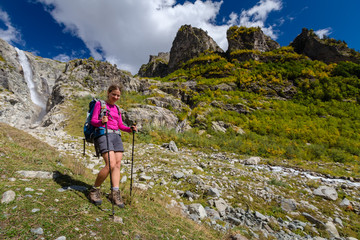 Naklejka na ściany i meble Woman trekking in Caucasus mountains against high waterfal in Us