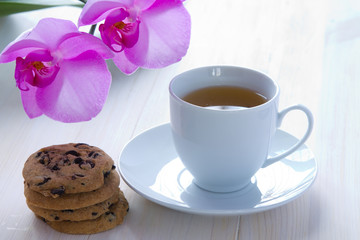 A cup of green tea with orchid flowers, homemade chocolate chip cookies