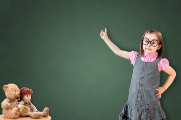 Cute little girl wearing business dress and show something on green chalk board.