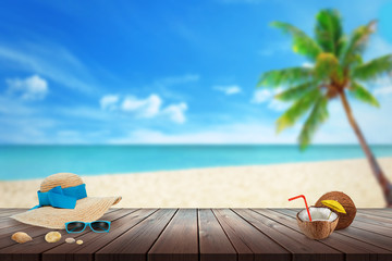 Hat, sunglasses, coconut, shell on beach table. Free space for text. Beach, sea, palm and blue sky in background.