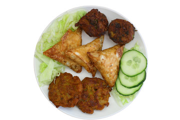 Indian snacks including samosas, onion bhajis and pakoras on plate isolated on white
