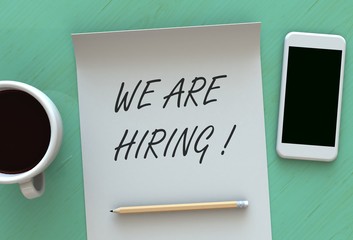 WE ARE HIRING, message on paper, smart phone and coffee on table