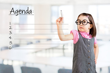 Cute little girl wearing business dress and writing blank agenda list. Office background.