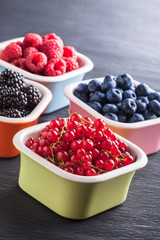 Berries colorful mix in four ceramic jars on black table in studio