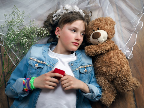 Girl teenager treats wedding accessories. Girl lying on the floor. In the picture, wedding veil, a teddy bear, a box for an engagement ring