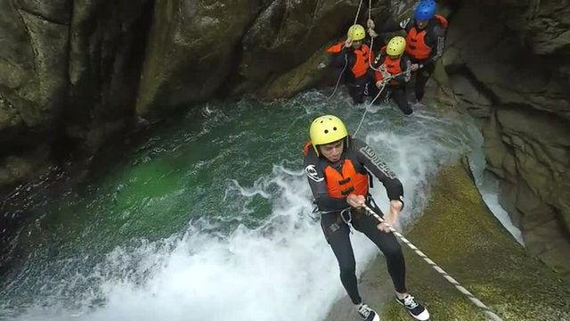 A group of adventurers in safety gear rappel down a cascading waterfall in a narrow moss-covered canyon near Banos, Ecuador, one descending as others wait above in lush green jungle.