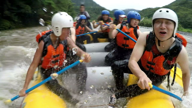 Experience thrilling whitewater rafting with a diverse group of Asiatic individuals,capturing the exhilarating moment in slow motion through an onboard camera as they get drenched by a massive wave.