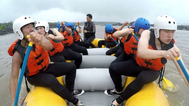 Experience the thrill of whitewater rafting with a group of nine energetic Asiatic people rowing at full speed,captured on board camera with sound.