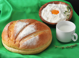 Round loaf of bread, milk in a Cup and the flour