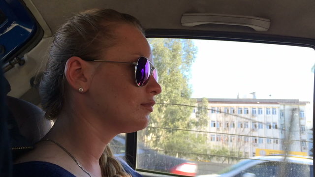 Beautiful girl with glasses in the role of a passenger looking out the car window. Sunny day. Close-up.