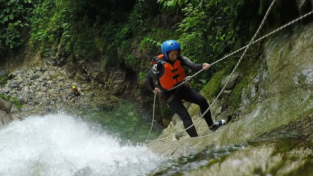 Experience the exhilarating sight of adult women rappelling down a massive waterfall in the breathtaking Andes rainforest,captured in a stunning static camera shot from above.