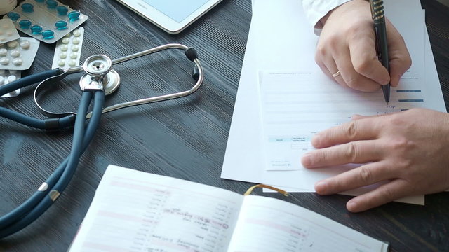 Male doctor writing rx prescription at the table, close