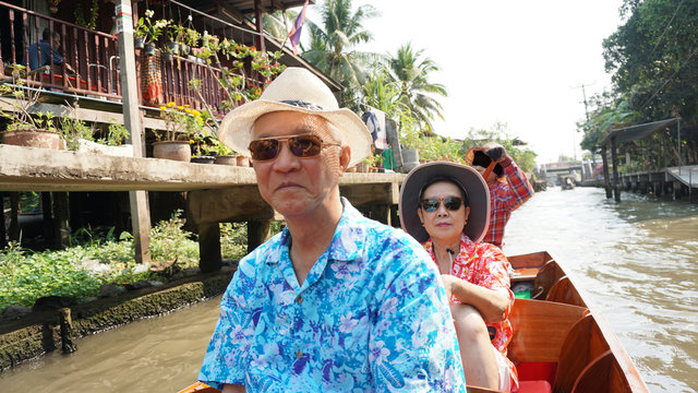Chinese Asian senior couple travel to thailand cruising on the boat in floating market