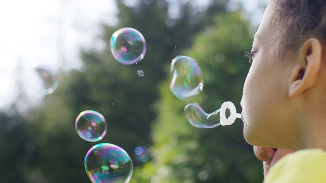 Close shot of young girl blowing bubbles outside, in slow motion