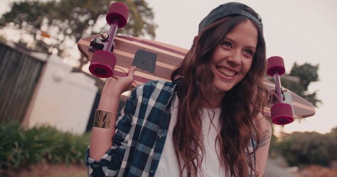 Skater girl standing with her board on her shoulders smiling