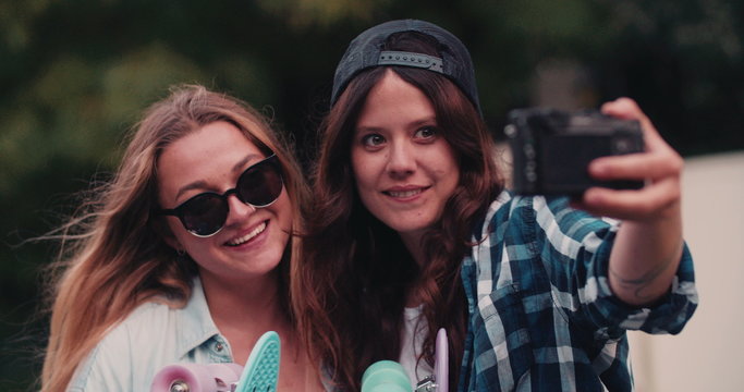 Hipster teen girls taking a selfie together with skateboards
