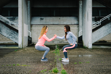 Two fitness women doing squat exercise workout outdoor on rainy winter day. Female athletes...