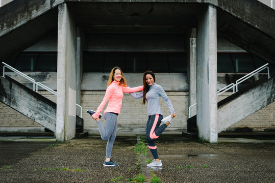 Two Fitness Women Stretching Legs And Quadriceps Together For Warm Up Before Running. Female Sporty Friends Exercising And Working Out.