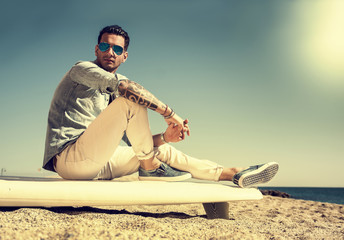Handsome man sitting on surfboard at beach - Powered by Adobe