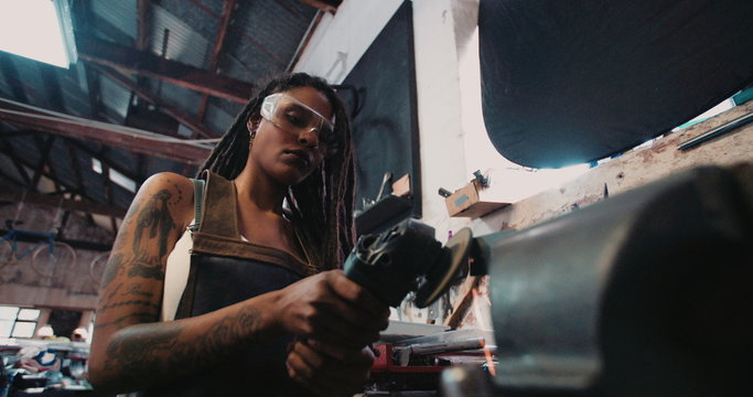 Skilled woman craftsperson with safety goggles using grinder on metal