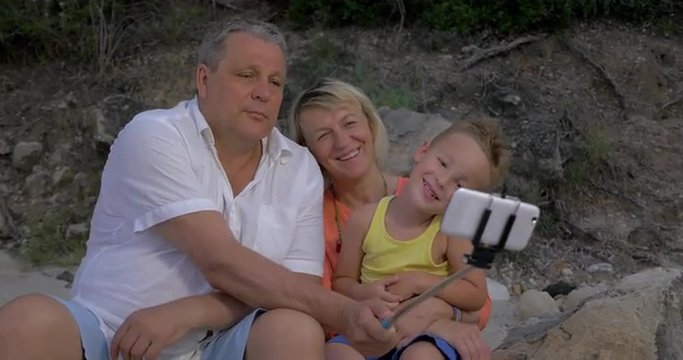 Little boy and his grandparents are taking selfie shots at smartphone with monopod stick, they are enjoying the process.