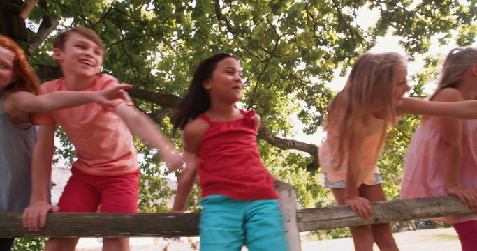 Children playing on a rustic wooden fence in a park