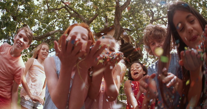 mixed race person of children blowing handfuls of colorful confetti