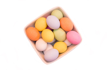 Colored eggs on a square bowl on a white background seen from above