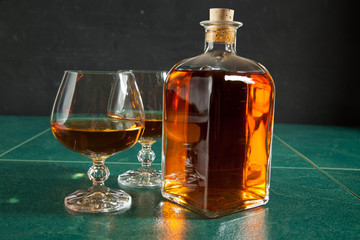 Two glasses of brandy and bottle on a green table top