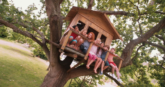 Row of children sitting on a wooden treehouse