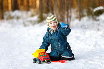 Fototapeta na wymiar Funny boy with toy car sitting on the snowy road