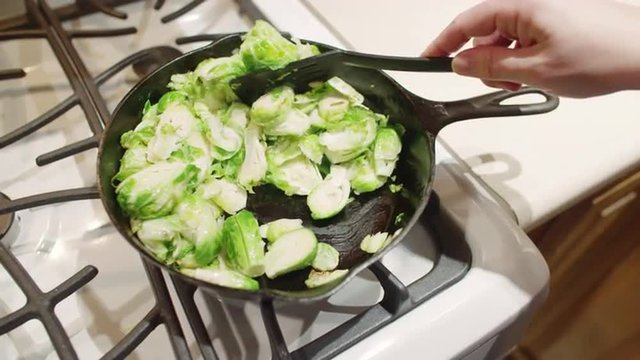 High angle view on pan of sliced sprouts, cooking on a gas stove.  Hand held camera with bright lighting.  Slow motion recorded at 60fps.
