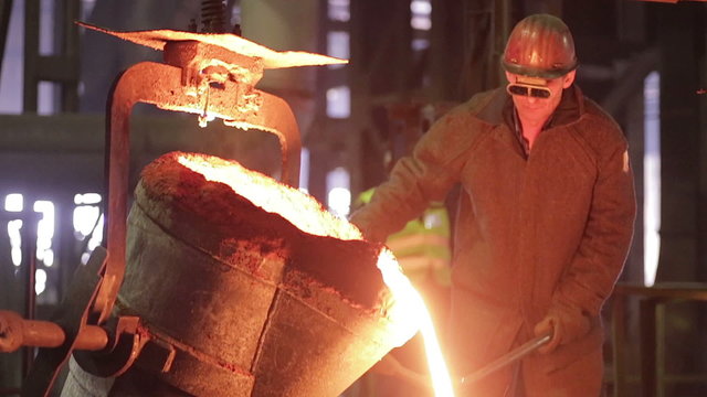 Worker on steel plant operates with  molten metal. HD.