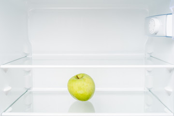 Green apple in empty refrigerator. Diet and hunger concept