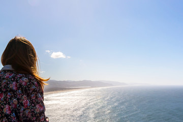 girl seen from the back with long hair and a hipster flowery coat looking at the ocean and the west coast of the united states of america during a sunny day