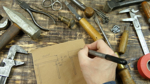 Man draws a draft. Indicates dimensions. Vintage tools on background