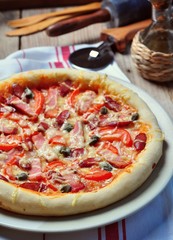 Home pizza with smoked meat and sausage, capers and tomatoes.