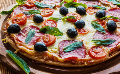 Pizza with salami, black olives and tomatoes on the wooden table.